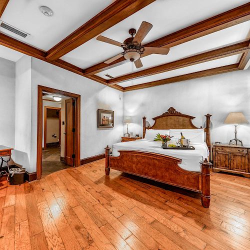 A bedroom with a wooden bed, desk and chair, ceiling fan, wooden floors, artwork, and a striped window covering.