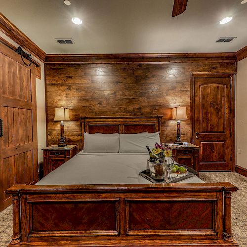A cozy bedroom with wooden furnishings, a bed with a tray of flowers, bedside lamps, a barn-style sliding door, and a round mirror on the wall.