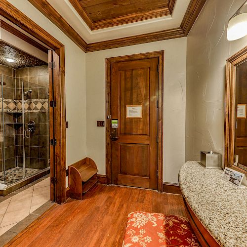A luxurious bathroom with a walk-in shower, wooden cabinets, seating, a large mirror, and elegant lighting. The room features a warm, cozy ambiance.