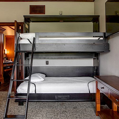 A room with a black bunk bed, ladder, wooden desk with magazines, and a door visible in the background ending the sentence.