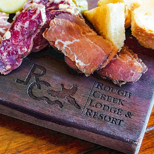 A charcuterie board with various cured meats and bread is displayed. The board is engraved with "Rough Creek Lodge & Resort."
