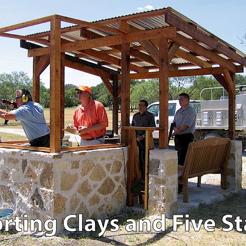Four people are at a shooting range with a covered shooting station. One person is aiming a shotgun. Text reads "Sporting Clays and Five Stand."