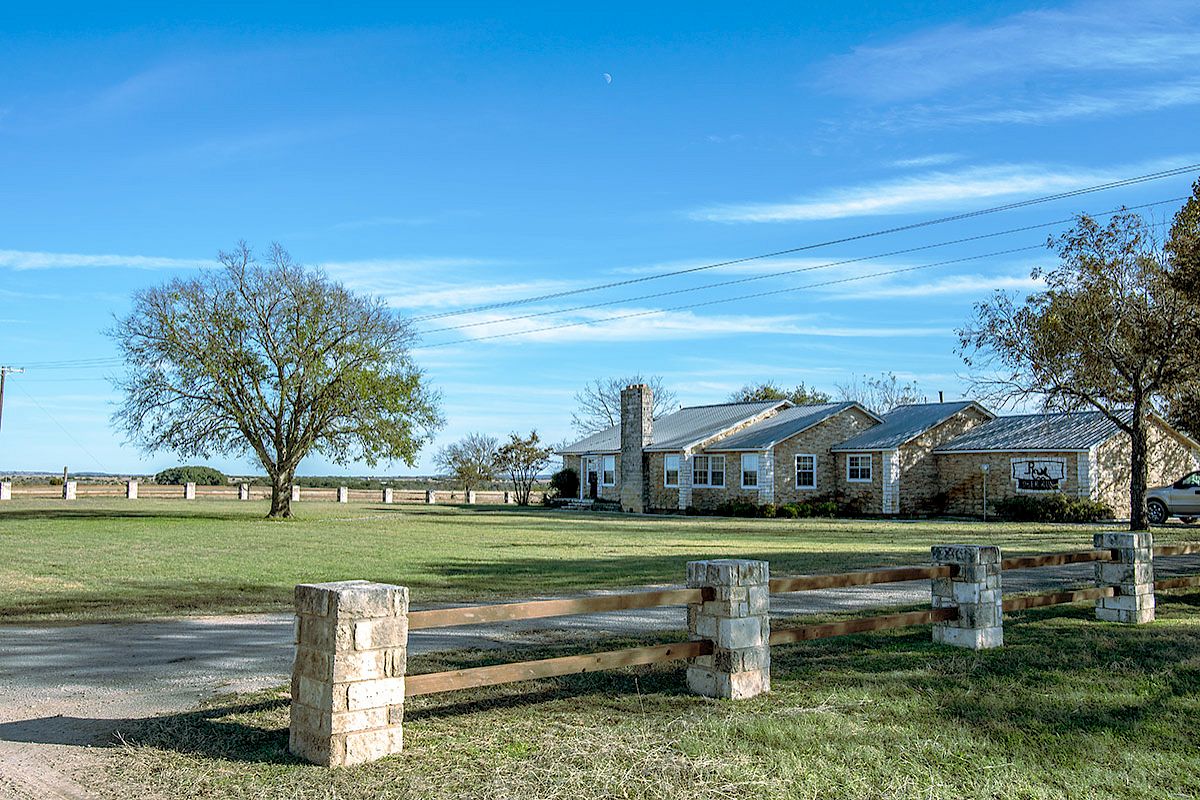A countryside scene with a house, large grassy yard, trees, and wooden fence under a clear blue sky.
