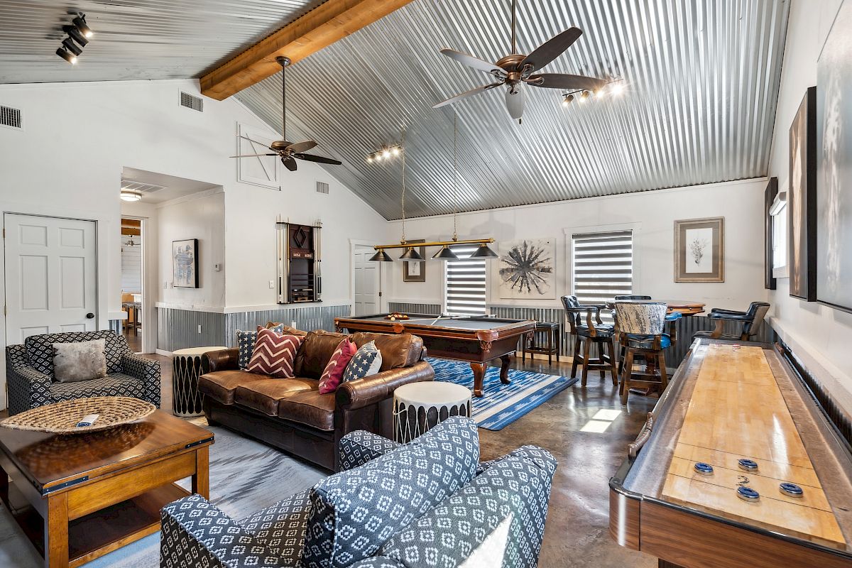 A stylish game room with a pool table, shuffleboard, seating, wooden accents, and ceiling fans.