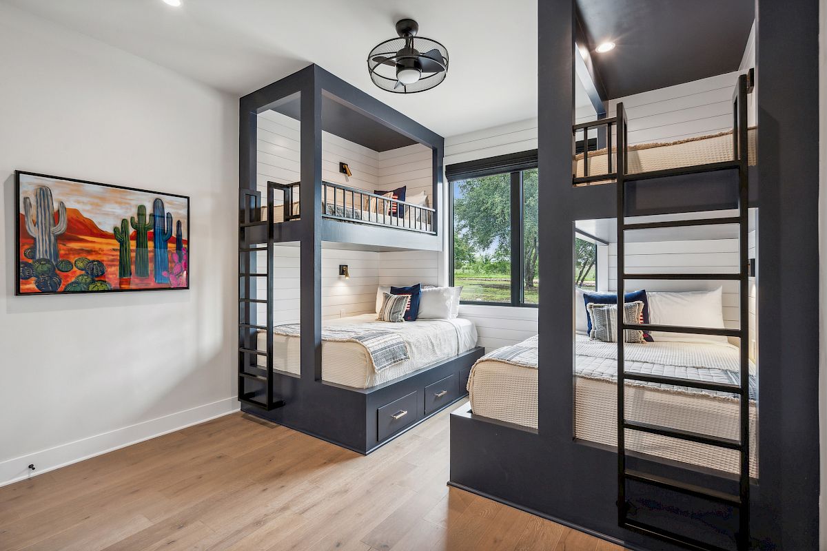 The image shows a modern room with double bunk beds, a ceiling fan, a window with a view, and a colorful cactus-themed artwork on the wall.