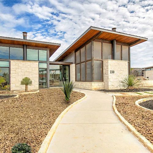 A modern house with extensive glass walls, a clean pathway, desert landscaping with palm trees, and a clear sky background.