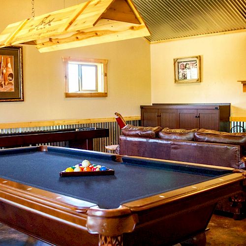 A cozy game room with a pool table, leather couch, wall-mounted TV, and framed pictures, creating a relaxing and inviting atmosphere.