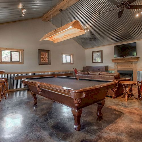 A rustic game room with a pool table, bar stools, TV, and decor.