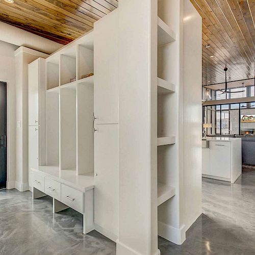 This image shows a modern interior with polished concrete floors, white built-in shelving, wooden ceilings, and large windows for natural light.