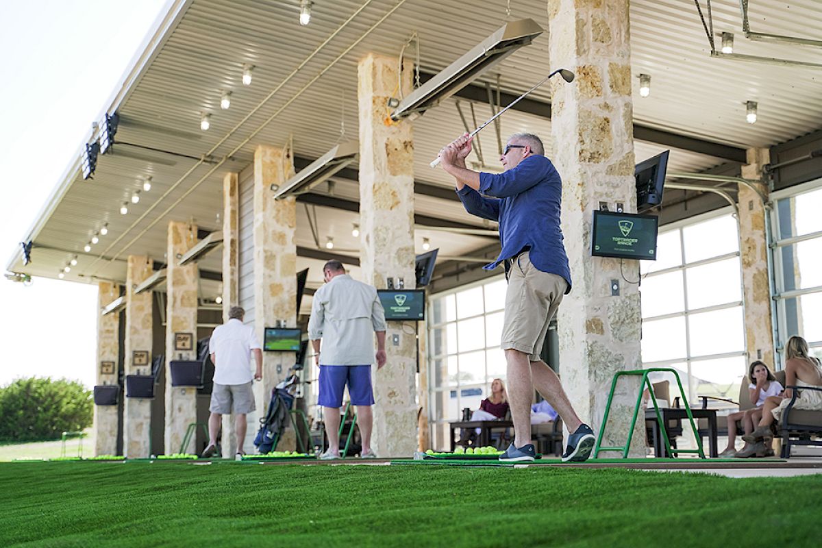 People are engaged in golfing activities at a driving range. Others are observing or preparing for their turn while enjoying the facility.
