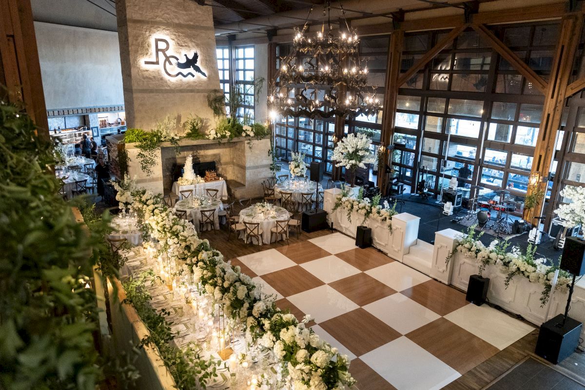 A beautifully decorated event space with elegant floral arrangements, a checkered dance floor, and chandeliers, creating a sophisticated ambiance.