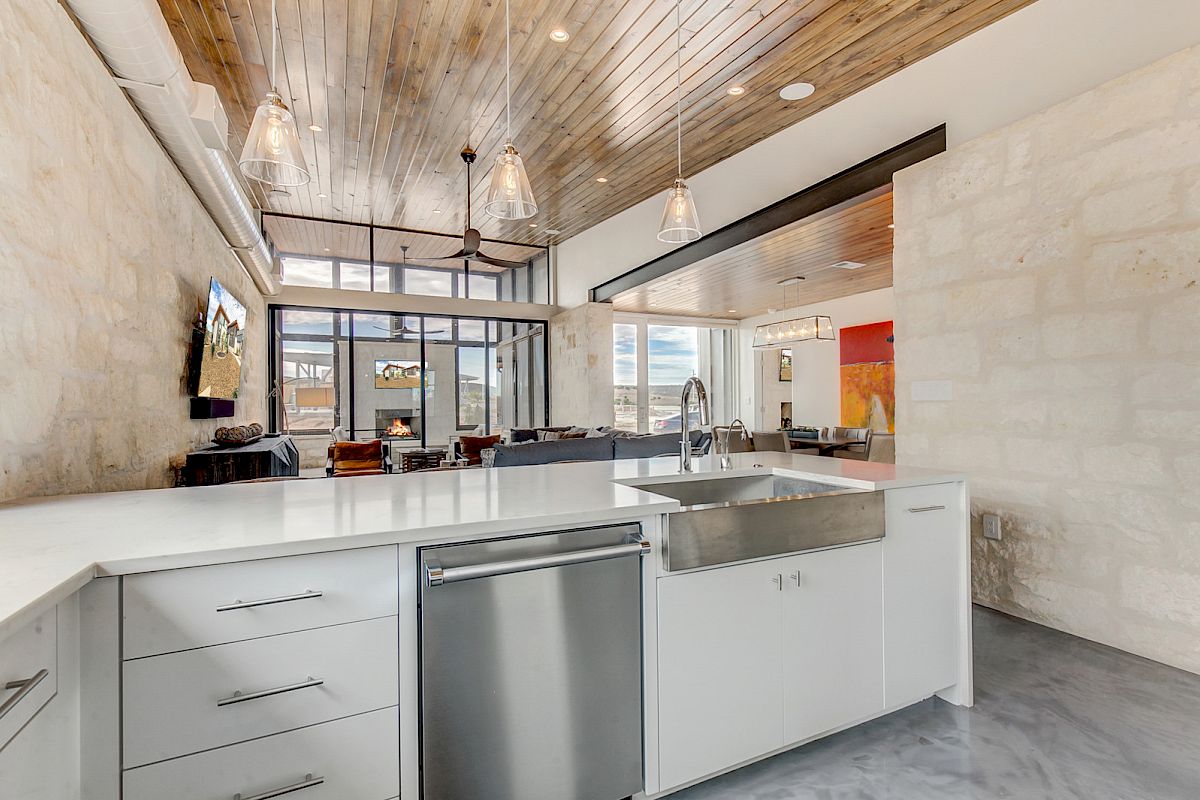Modern kitchen and living area with wood ceiling, pendant lights, marble countertop, and large windows. Cozy and stylish interior.