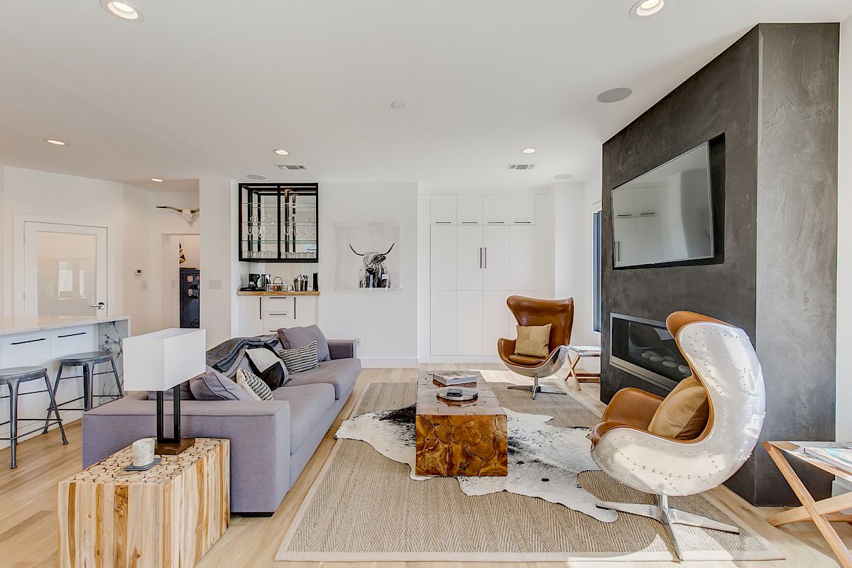 A modern living room with a gray couch, wooden accents, leather chairs, and a large TV above a dark fireplace.