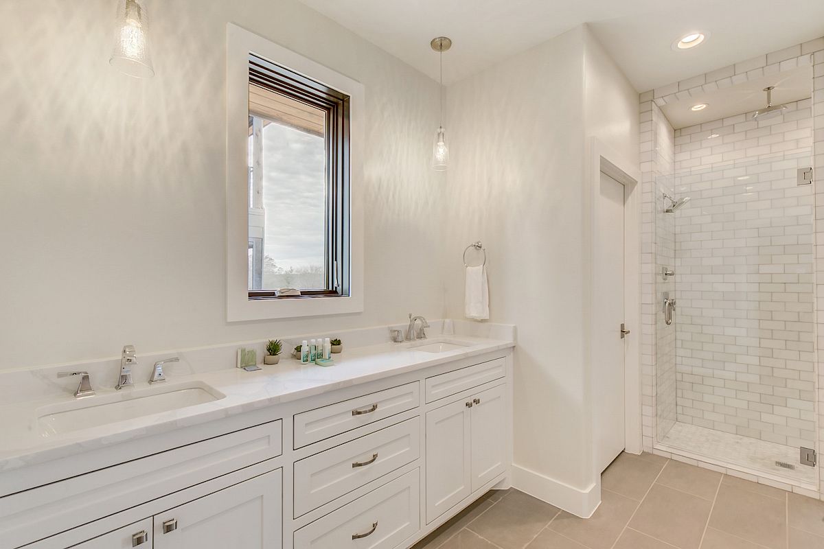 A modern bathroom featuring a double vanity, white cabinetry, a towel ring, and a glass-enclosed shower with subway tiles.