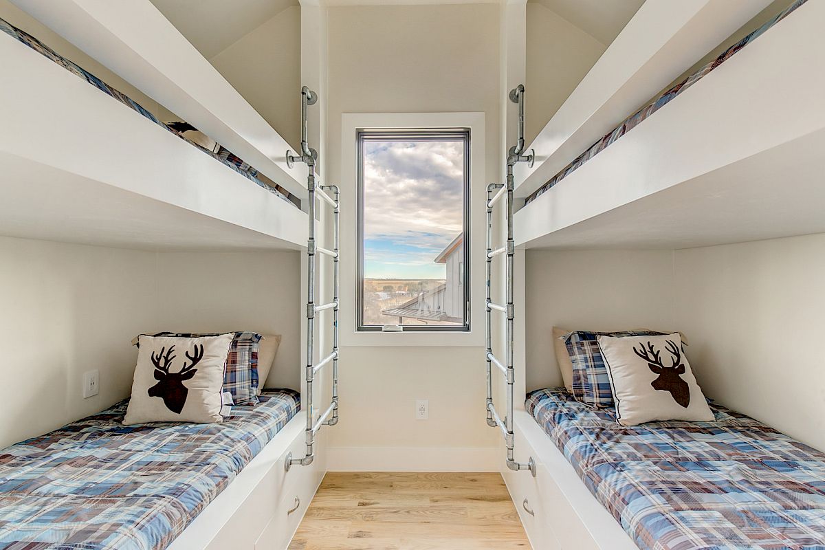 A room with two sets of bunk beds, plaid bedding, and pillows with a deer silhouette. There's a window with a scenic view in the middle.