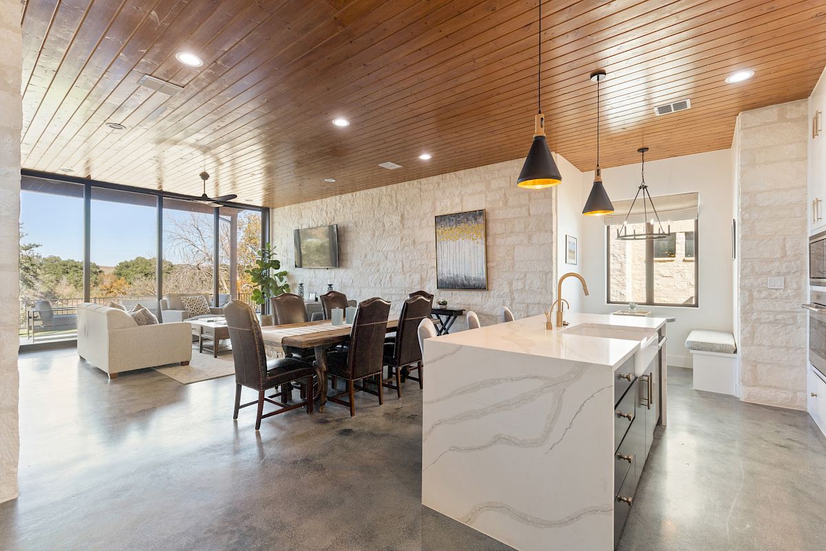 A modern open-concept kitchen and dining area with high ceilings, pendant lights, and large windows offering a scenic view.