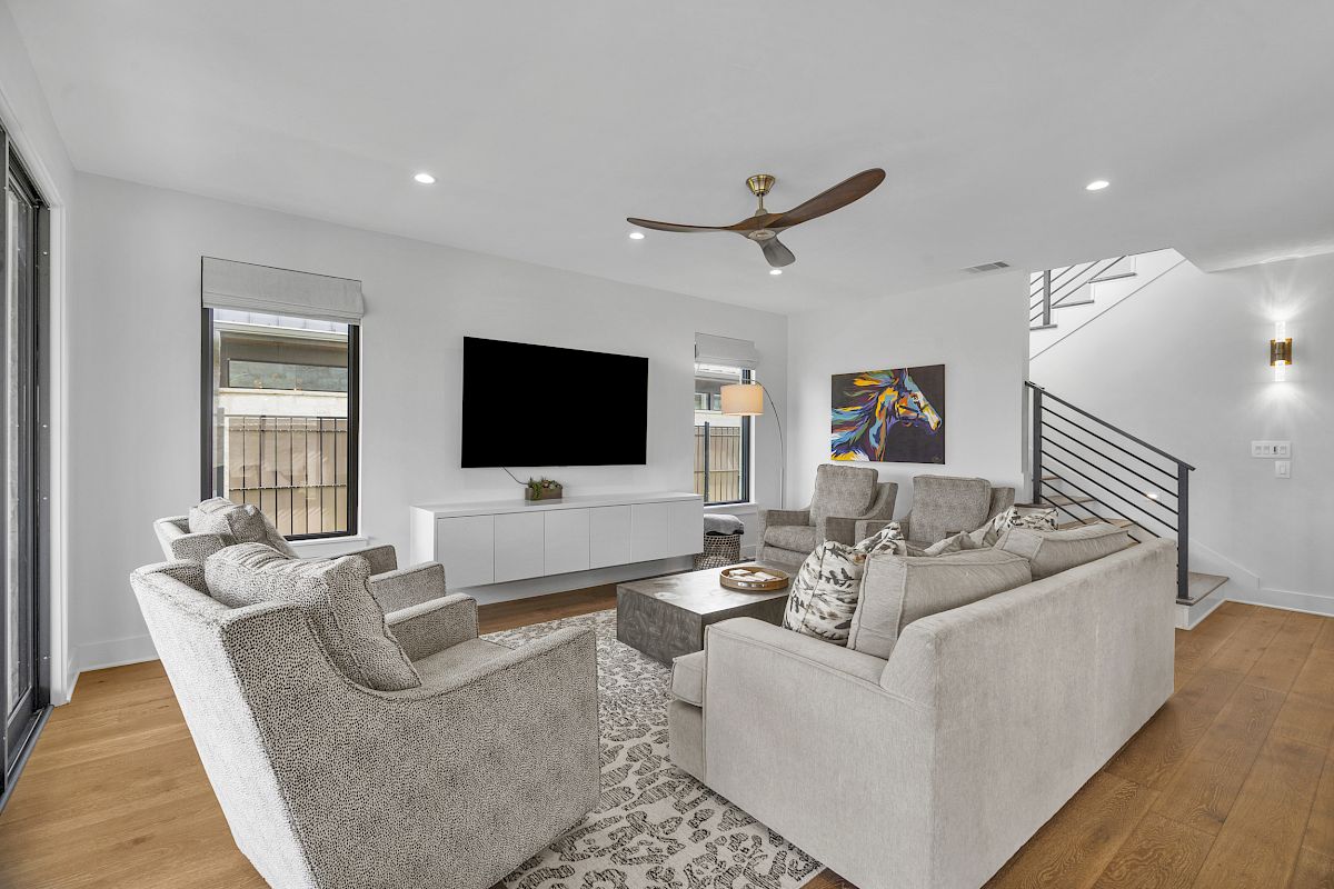 A modern living room with gray sofas, a coffee table, wall-mounted TV, abstract art, wooden floor, and a ceiling fan.