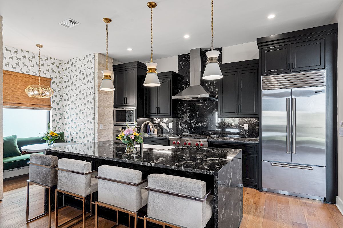 Modern kitchen with black cabinets, marble island, pendant lights, stainless steel appliances, and hardwood floor.