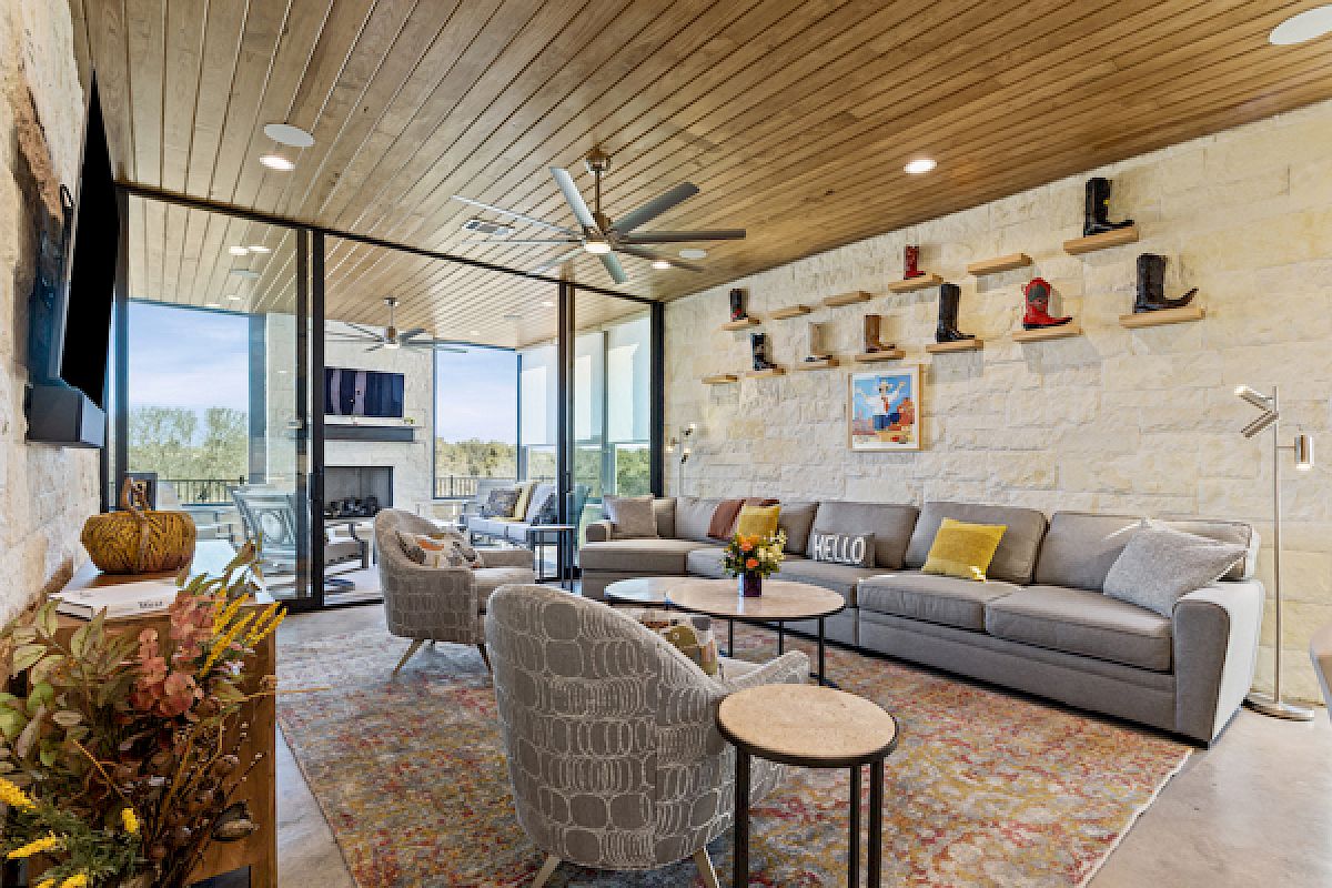 A cozy living room features a modern design, ample seating, ceiling fans, decorative boots on shelves, and a view of an outdoor patio.