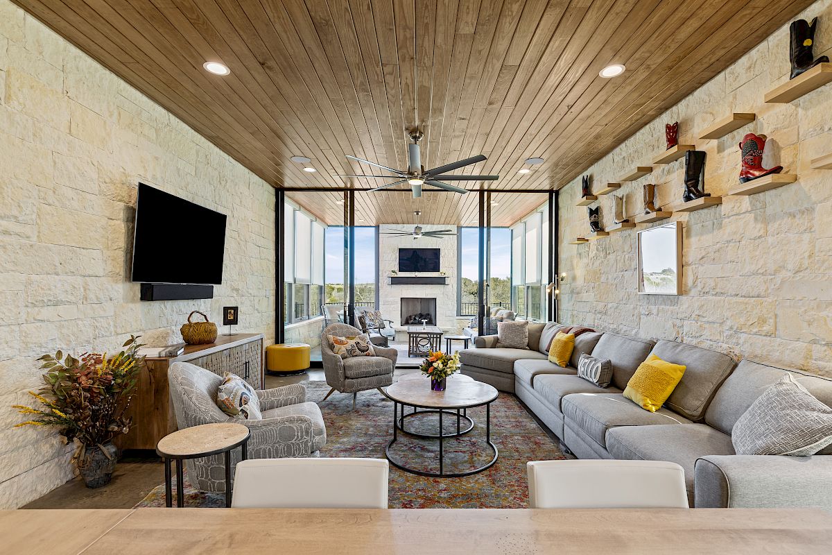 A cozy living room with a large sectional sofa, TV, fireplace, and boots displayed on shelves; warm tones and ample natural light.