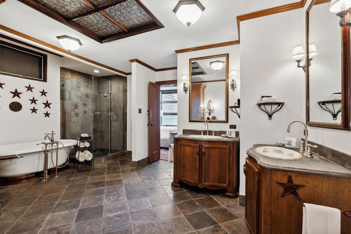 A bathroom with a bathtub, glass shower, dual sinks, star decorations, and brown cabinetry on tiled flooring.