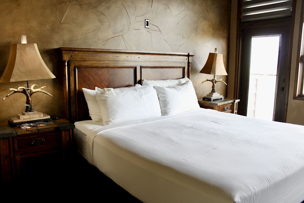 A neatly made bed with white linens in a room with a wooden headboard and nightstands, featuring decorative lamps.