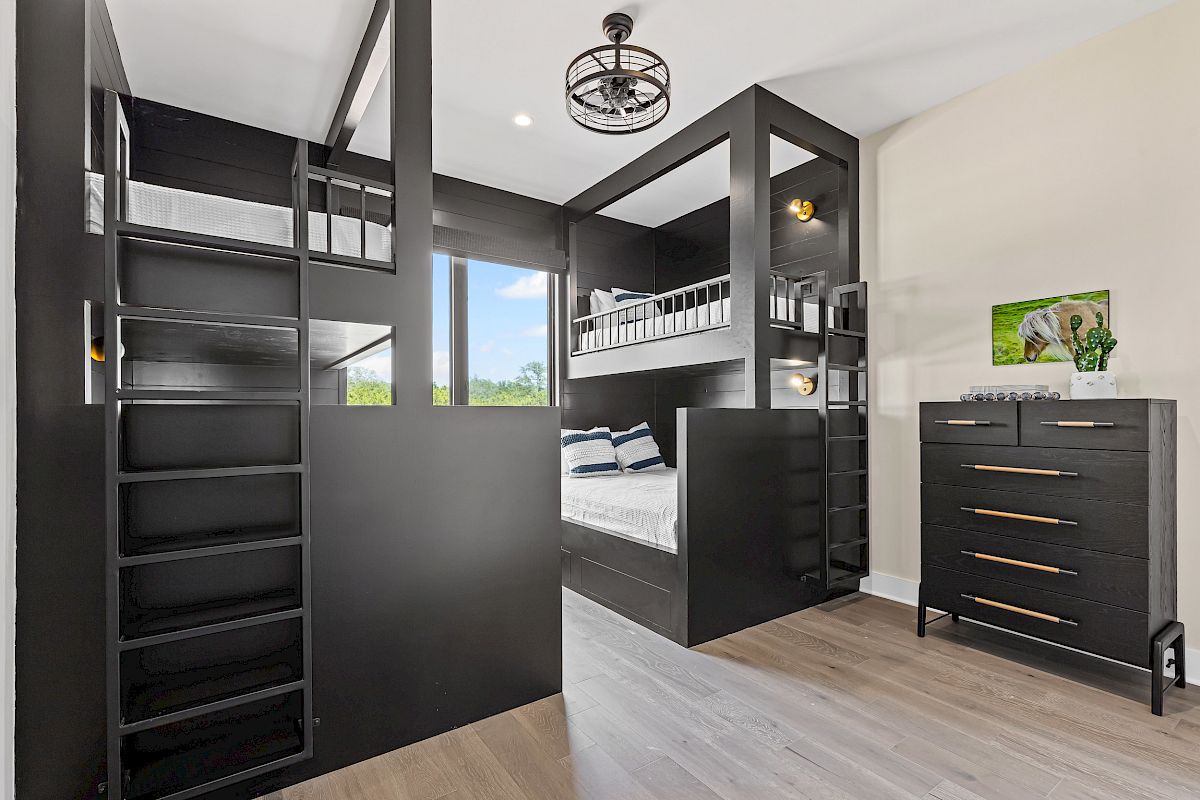 The image shows a modern bedroom with black bunk beds, a dresser, and artwork on the wall, featuring minimalist and sleek design elements.
