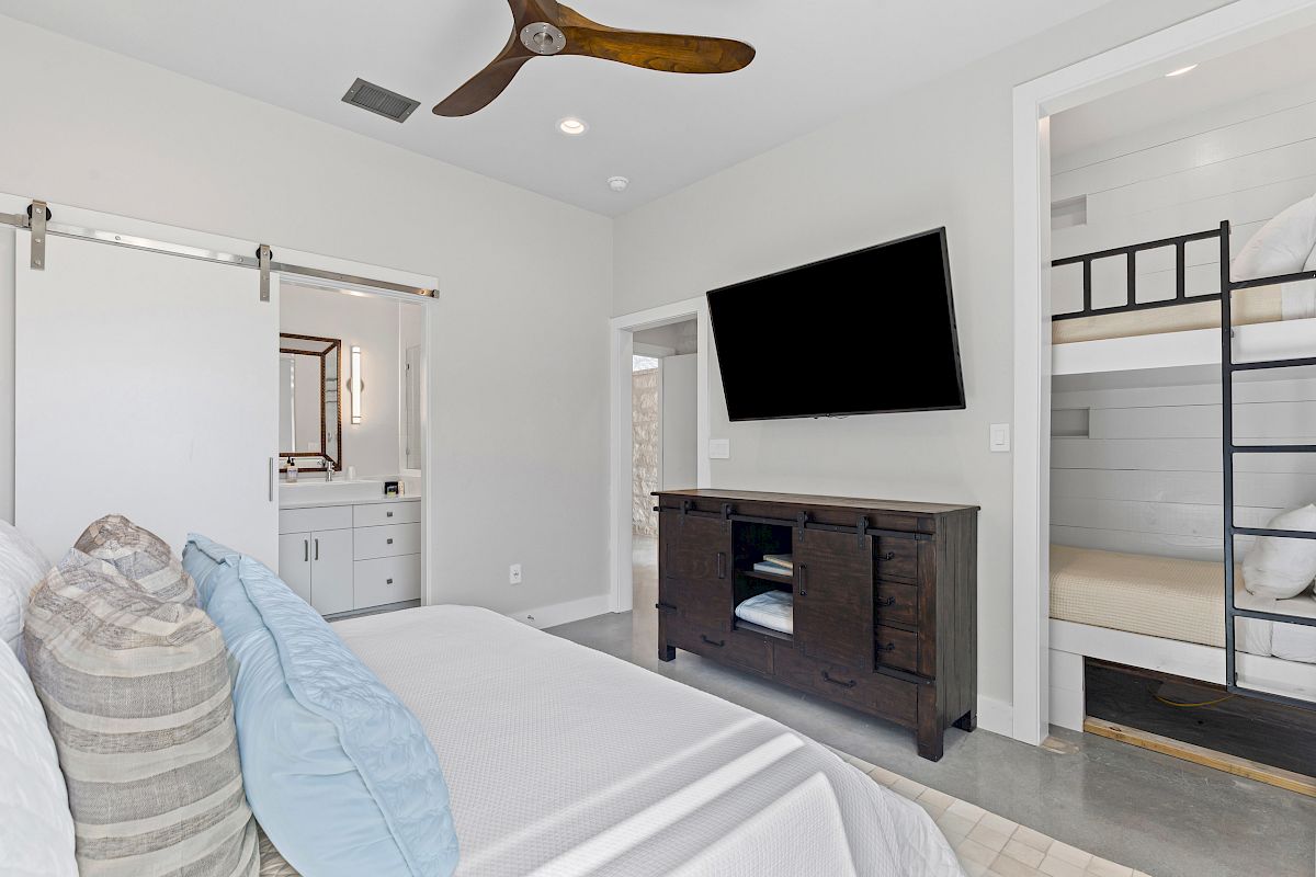 The image shows a bedroom with a bed, TV, dresser, bunk beds, and a sliding door leading to a bathroom.