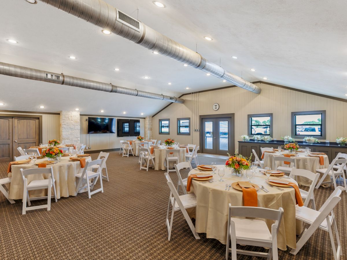 The image shows a decorated banquet hall with round tables, flowers, and folded napkins, ready for an event.