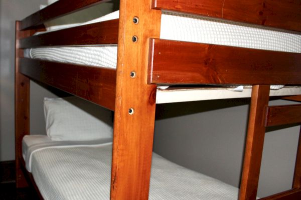 The image shows a wooden bunk bed with white bedding.