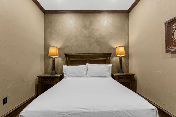 A cozy bedroom with a large bed, two bedside tables, each with a lamp, and beige textured walls create a warm, inviting atmosphere.