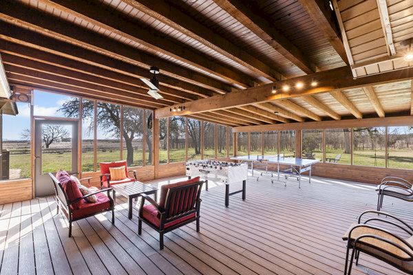 A spacious sunroom with a wooden ceiling and floor, featuring casual seating, a foosball table, and a view of the outdoors.