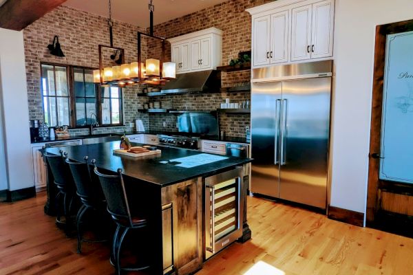 A modern kitchen with wooden flooring, a large island, stainless steel appliances, skylights, and exposed brick walls in warm tones.