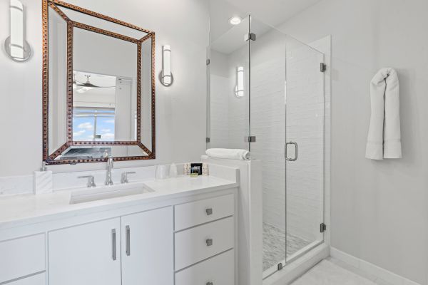 The image shows a modern bathroom with a glass shower, white vanity, large mirror, and towels, creating a clean and minimalist design.