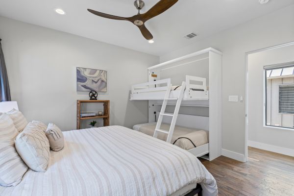 The image shows a bedroom with a large bed, bunk beds, a ceiling fan, artwork, and a window, all in a modern and clean style.