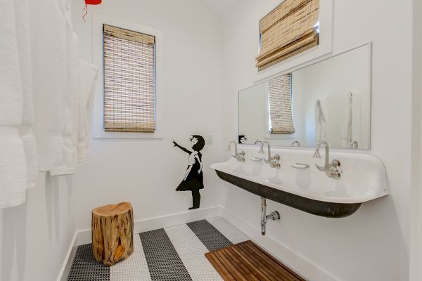 The image shows a bathroom with a mural of a girl reaching for a balloon, a large mirror, dual sinks, striped floor, and rustic wooden stool.