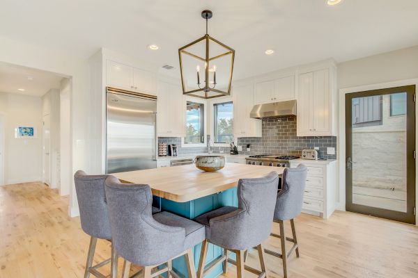 A modern kitchen with a central island, gray chairs, pendant lighting, stainless steel appliances, and light wood flooring.
