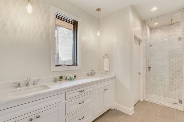 A modern bathroom with a double sink vanity, white cabinets, a window, and a glass-enclosed shower featuring white subway tiles.