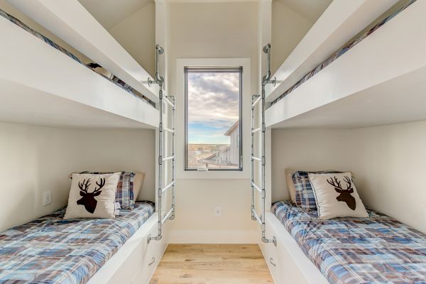 The image shows a room with two sets of bunk beds, each featuring deer-themed pillows and plaid bedding, and a window with an outdoor view.