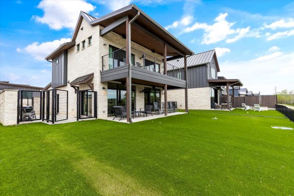 A modern two-story house with balconies and large windows, surrounded by a spacious lawn under a partly cloudy sky.