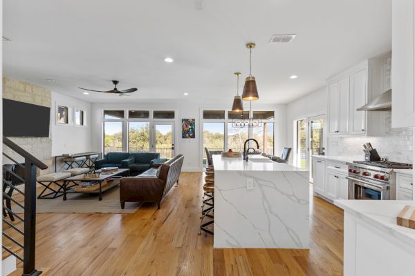A modern open-concept kitchen and living room with a marble countertop, leather sofa, and large windows offering natural light.