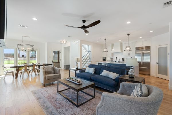 A modern open-concept living area with a kitchen, dining table, and seating, featuring neutral tones and natural light.