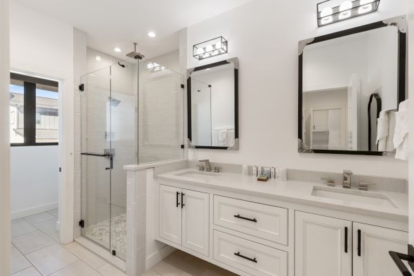 A modern bathroom with a glass shower, dual sinks, mirrors, and sleek lighting fixtures.