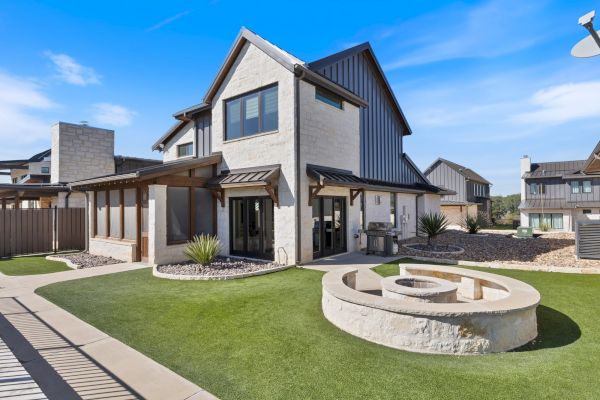 A modern house with a stone exterior, a manicured lawn, and a circular stone structure in the yard under a clear blue sky.