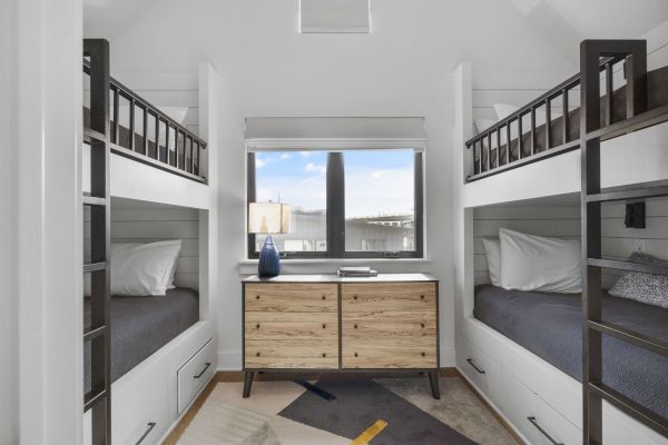 The image shows a cozy room with two bunk beds, a wooden dresser, and a window with a view, creating a compact and functional space.