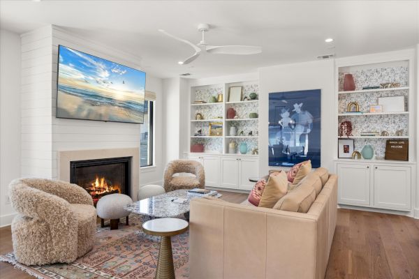 A cozy living room with a fireplace, TV, beige sofa, fluffy chairs, and built-in shelves adorned with decor items and artwork.