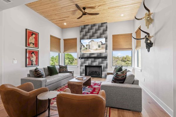 A modern living room with gray sofas, brown chairs, a patterned fireplace, and a wooden ceiling, decorated with art and animal mounts.