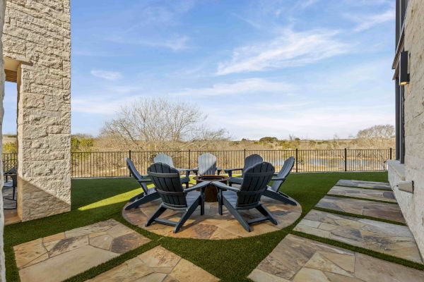 A patio with six chairs arranged in a circle on stone pavers, surrounded by a fence and scenic view.