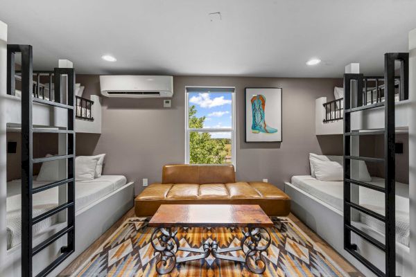 Room with two bunk beds, leather sofa, coffee table, air conditioning, rug, window, and boot artwork on the wall.