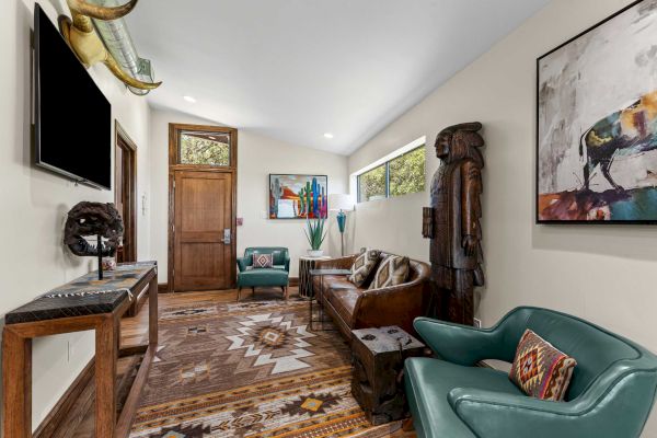 A room with Southwestern decor, featuring art, a patterned rug, a wooden sculpture, and teal chairs, creating a cozy vibe.